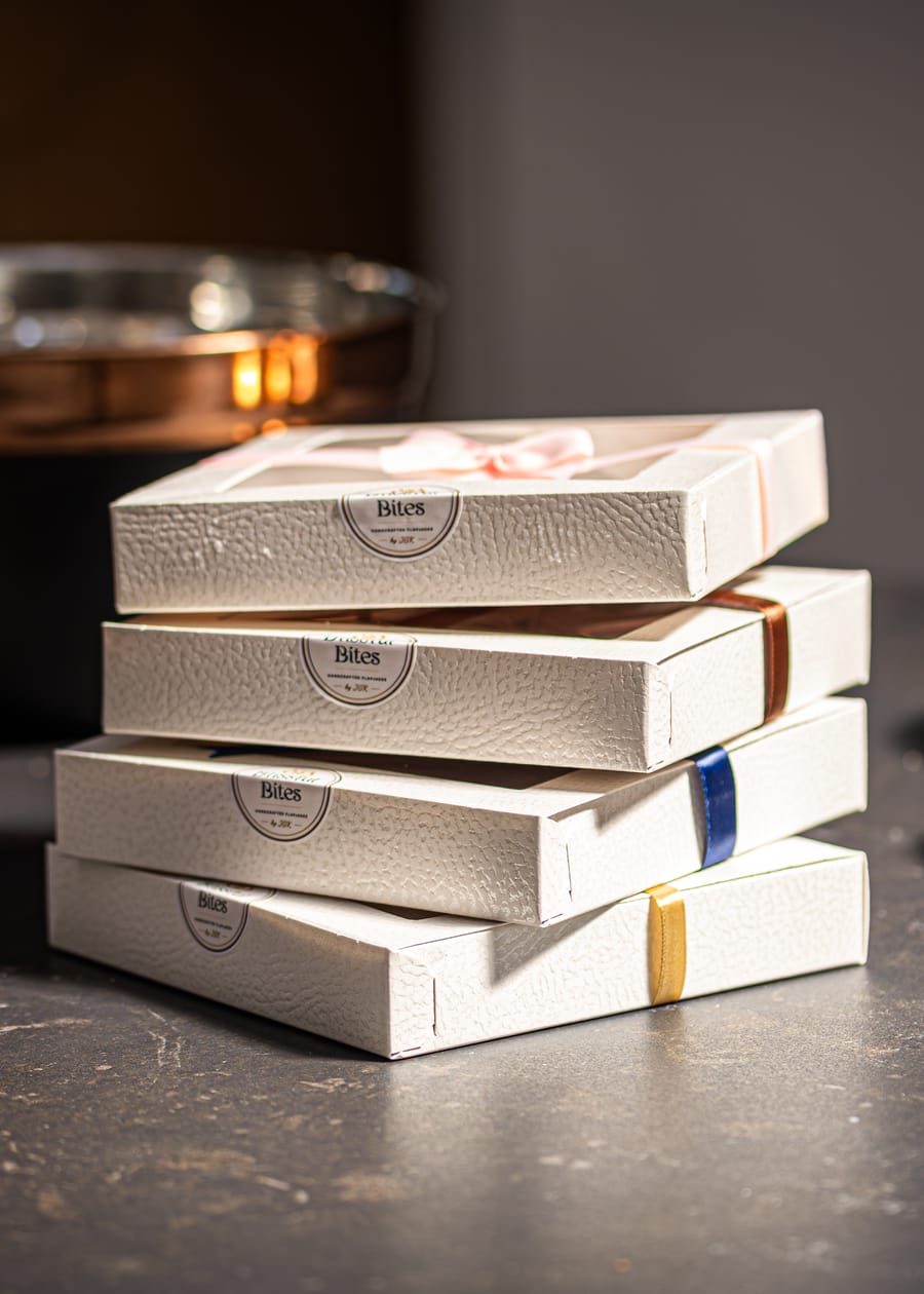 Stacked white window gift boxes, each banded with a different colour ribbon