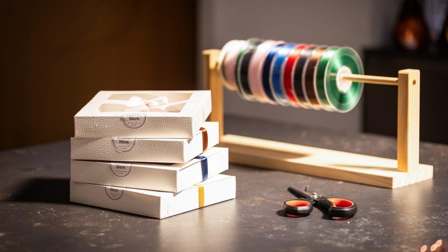 A rack of ribbon spools in a range of colours beside stacked gift boxes
